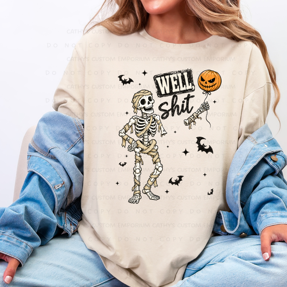 Cream sweatshirt featuring a wrapped mummy skeleton, flying bats, stars, a severed skeletal hand, and a jack-o-lantern balloon with the words Well Shit.