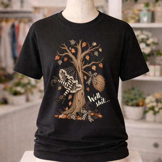 Black shirt featuring a vintage witch who crashed into an autumn tree with a broom, witch hat, gingham bows, and the phrase Well shit.