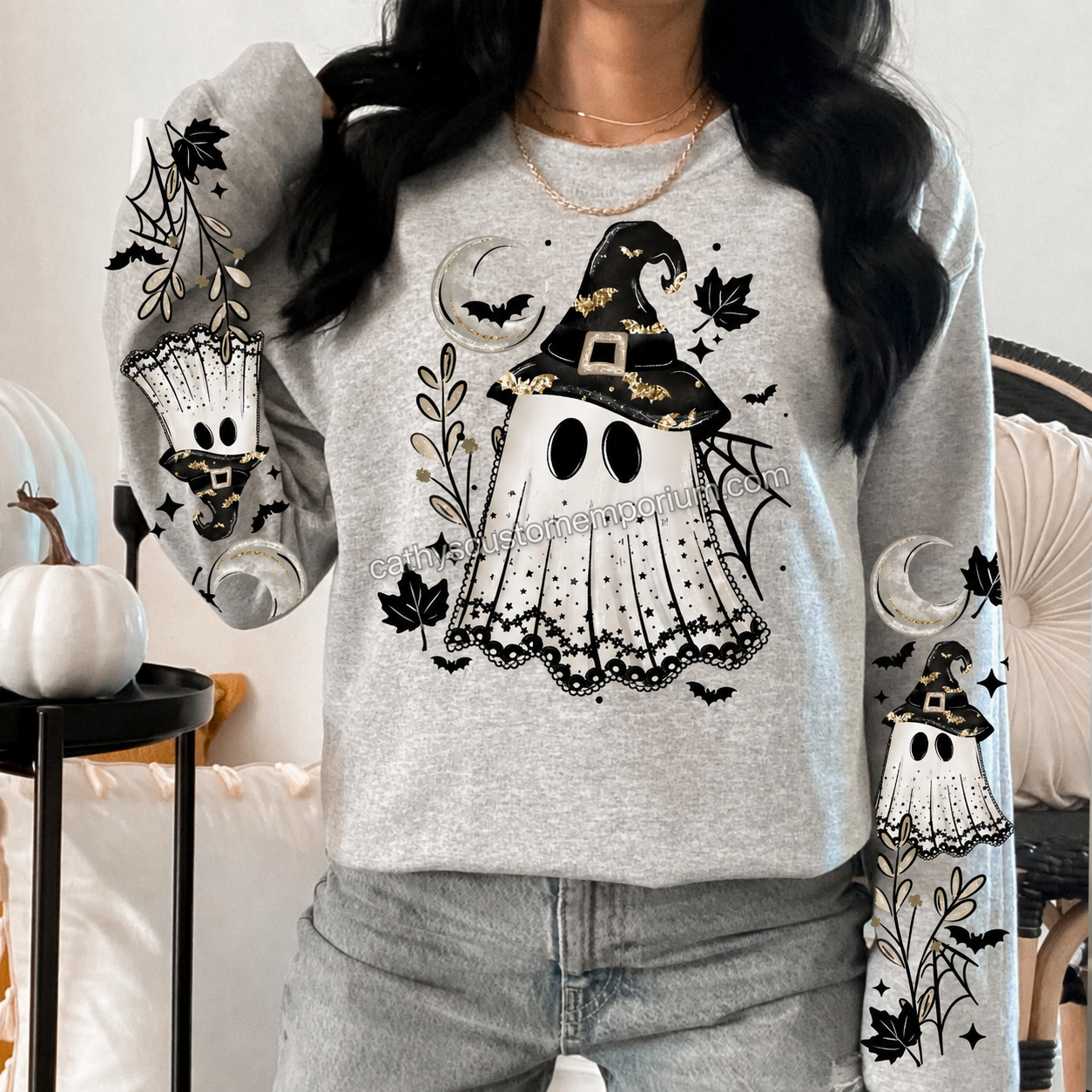 Woman wearing a gray Halloween sweatshirt with a witch ghost front graphic and coordinating ghost, moon, bat, web, and leaf sleeve designs