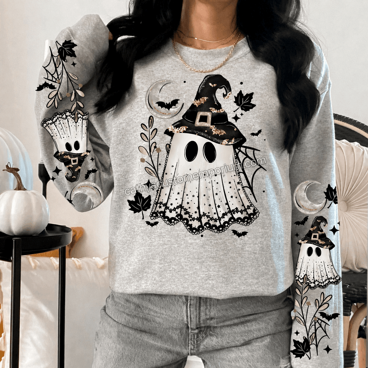 Woman wearing a gray Halloween sweatshirt with a witch ghost front graphic and coordinating ghost, moon, bat, web, and leaf sleeve designs